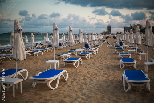 Loungers on sandy beach by the sea on a dramatic sky, end of season in resort, Bulgaria