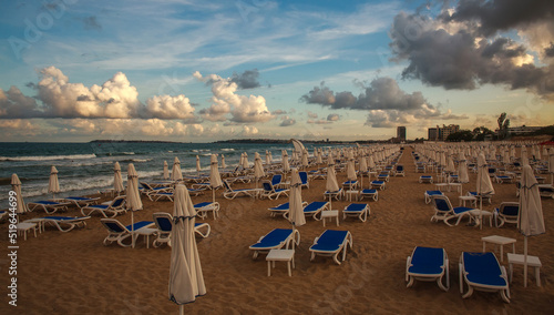 Loungers on sandy beach by the sea on a dramatic sky, end of season in resort, Bulgaria