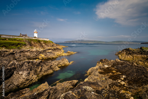 rocky shoreline with turquoise pools and the historic Broadhaven Lighthouse on a clifftop promontory