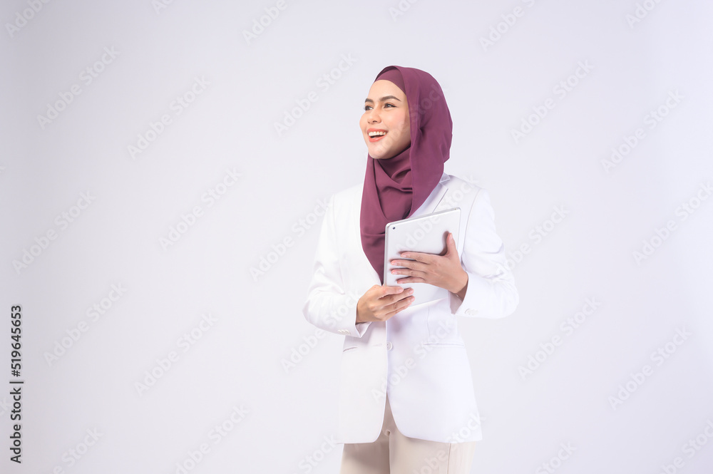 Beautiful muslim business woman wearing white suit with hijab holding tablet in studio. Beautiful muslim business woman wearing white suit with hijab holding tablet in studio.