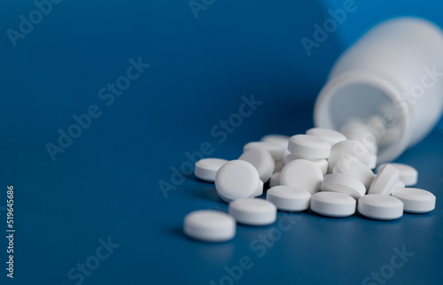 White pills poured out white bottle. White pills on a blue background.
