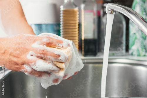 Young woman's hands washing a white cup with water and dish soap. Close-up of female hands rinsing a dirty used white mug with the tap running. Concept of cleanliness