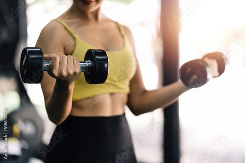 Beautiful Asian woman working out in the gym to stay fit and strong and gain beautiful muscles by lifting weights.