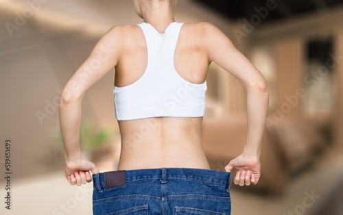 Young woman standing near bed in bedroom. Fat burning treatment of thick belly. Weight loss program, dieting.
