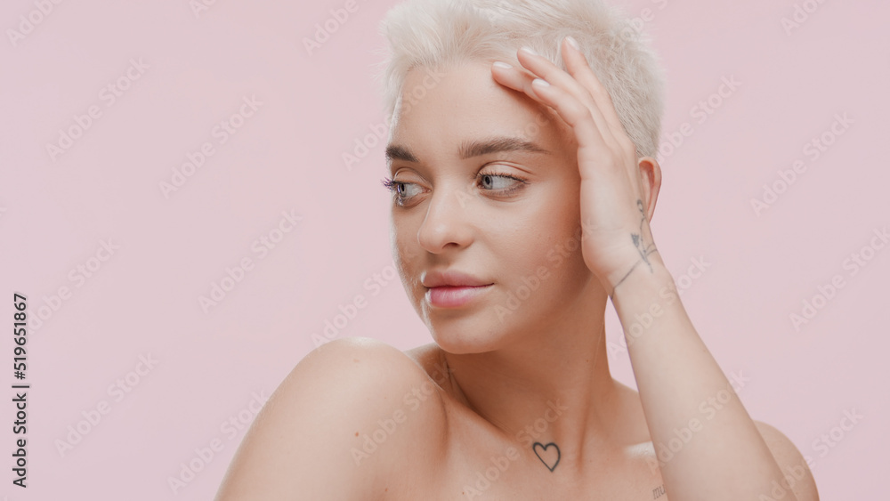 Pretty young slim Caucasian woman with short fair hair strokes her face looking away and smiling on pale pink background | Anti-acne concept Pretty young slim Caucasian woman with short fair hair strokes her face looking away and smiling on pale pink background | Anti-acne concept