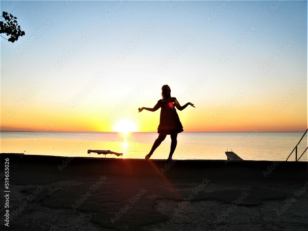 Tourism. Journeys. Sea. Beautiful sunset. Black silhouette of a girl in a dress.