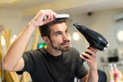Female hairdresser drying and combing his own hair in his hair salon