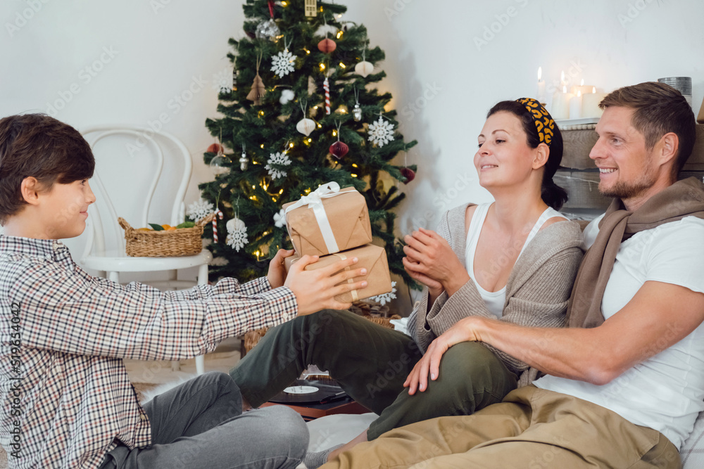 Happy parents receiving a Christmas gift from his son. Smiling child boy giving present to mom and dad at home. Happy parents receiving a Christmas gift from his son. Smiling child boy giving present to mom and dad at home.
