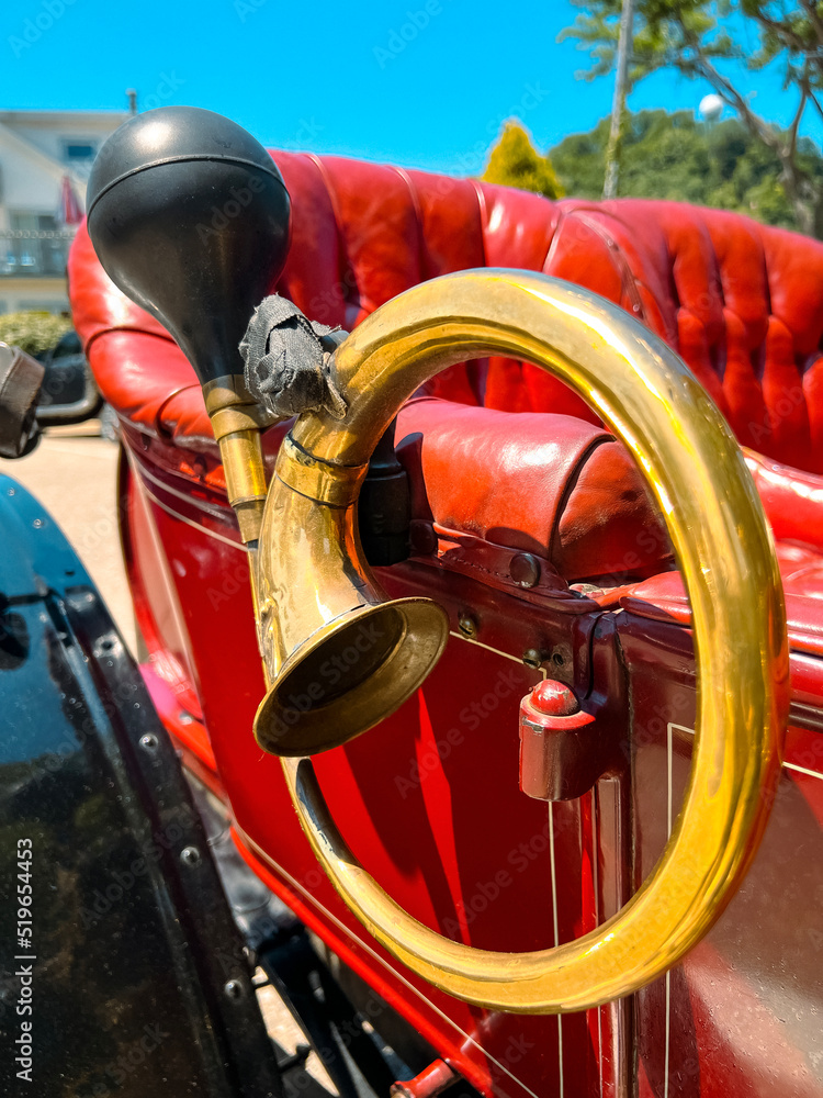 Closeup views of craftsmanship and details of a restored vintage classic car buggy. Round French horn attached to side in gold brass. Partial view of red leather interior.