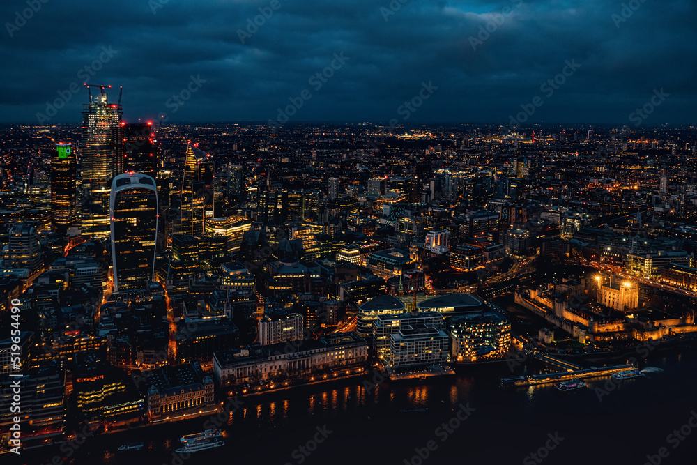 Aerial view of north London, blue hour just after sunset. Famous Tower visible in bottom right corner near river Thames. Orange yellow street lights starting to glow