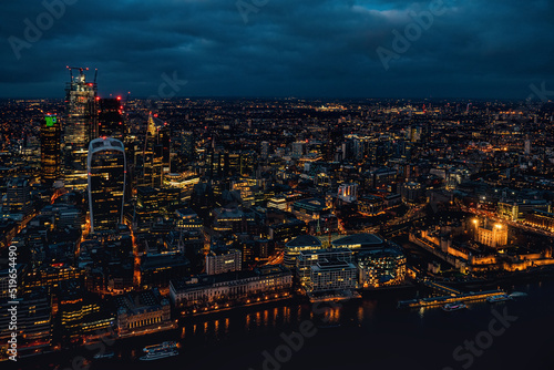 Aerial view of north London, blue hour just after sunset. Famous Tower visible in bottom right corner near river Thames. Orange yellow street lights starting to glow