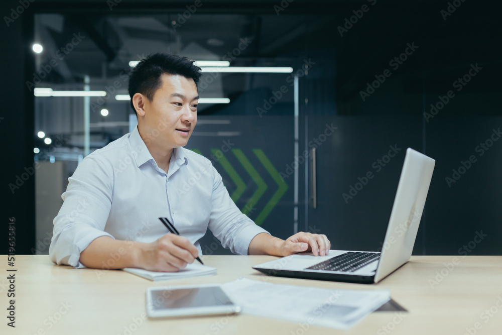 Young businessman, freelancer, Asian working with documents, writing with a pen, working on a laptop Sitting at a desk in a modern office Young businessman, freelancer, Asian working with documents, writing with a pen, working on a laptop Sitting at a desk in a modern office