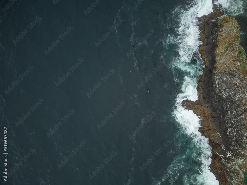 Shot from the air. Picturesque nature, seascape. Dark turquoise surface of the ocean and light white waves beating against the stone shore. Minimalism. Abstraction. Tourism, ecology.