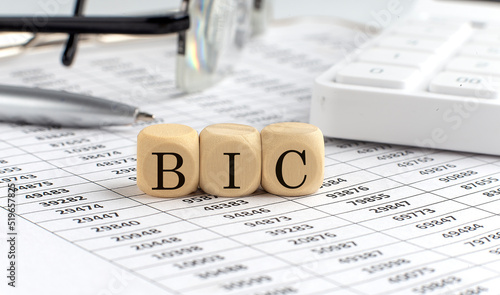 wooden cubes with the word BIC on a financial background with chart, calculator, pen and glasses, business concept.