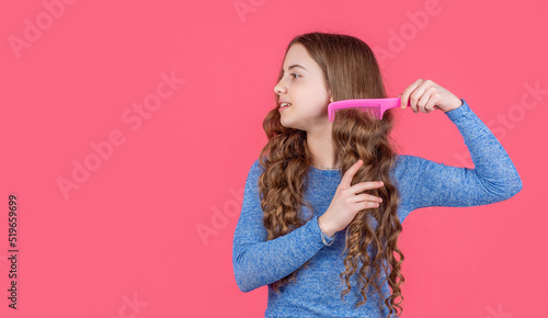 teen girl combing curly hair with hairbrush on pink background with copy space
