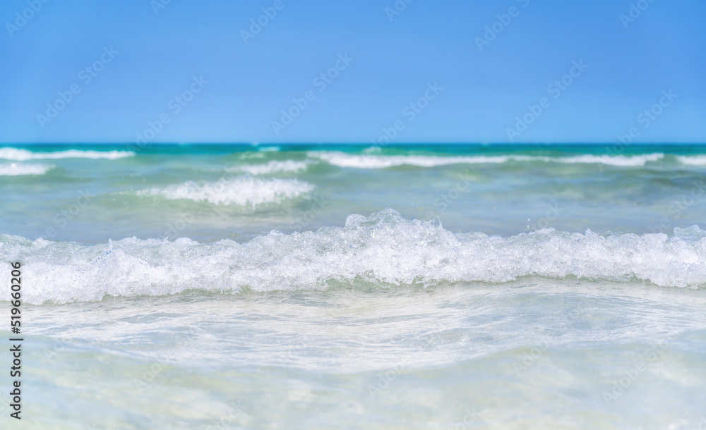 Kleine Wellen in einer türkis blauen Brandung eines tropischen Meeres vor wolkenlosem Himmel