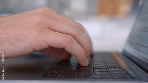 Side view of hands pressing keys of black laptop keypad. Action. Close up of a keayboard and man hands typing on modern computer on blurred background.