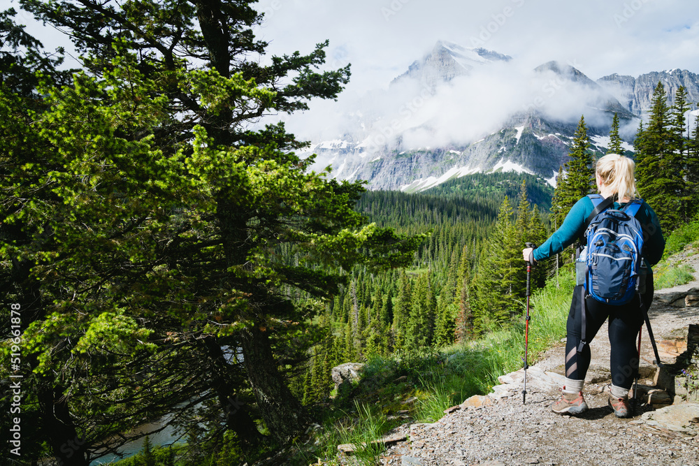 Blonde woman hiker takes a moment to enjoy the scenery along the Grinnell Glacier Hike in Glacier National Park Montana