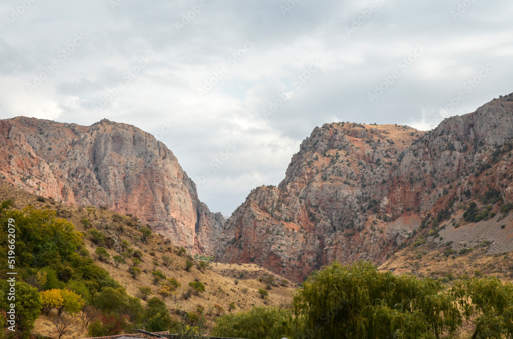 Red mountains and rocks covered green vegetation under cloudy sky in Armenia near Noravank monastery 