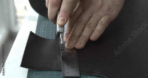 Working process of crafting a new handmade leather wallet in the leather workshop. Man's hands working with knife and iron ruler and cutting a leather.