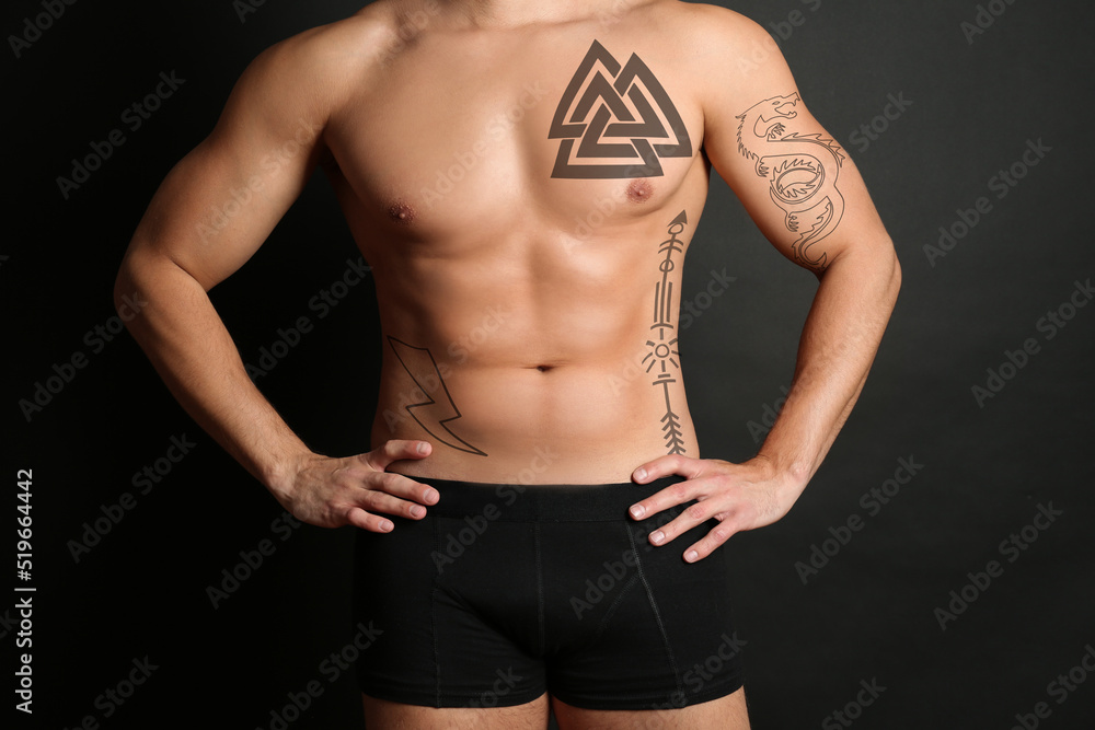 Fototapeta premium Handsome man with beautiful tattoo sketches on black background, closeup