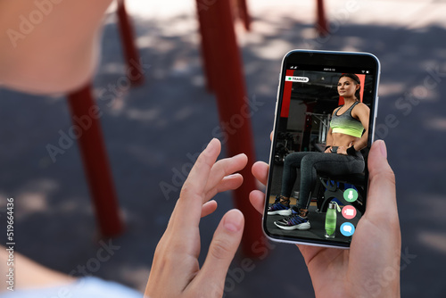 Woman having workout with personal trainer via smartphone outdoors, closeup