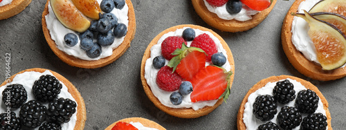 Delicious tartlets with fresh berries on grey table, flat lay. Banner design photo