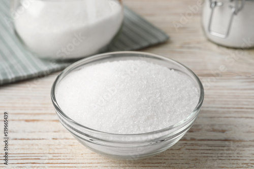 Granulated sugar in glass bowl on white wooden table, closeup