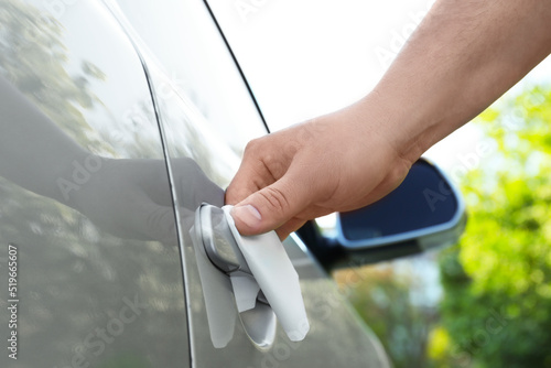 Man with napkin sanitizing car door handle outdoors, closeup