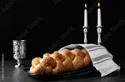 Foto Homemade braided bread with sesame seeds, goblet and candles on dark grey table