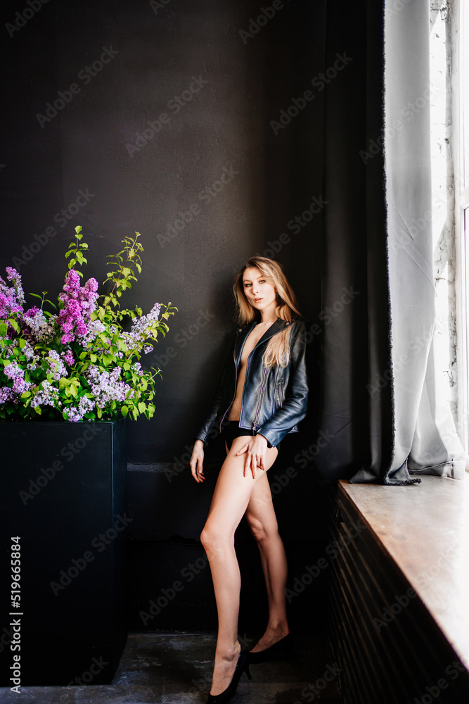 a blonde in panties and a leather jacket by the wall with a bouquet of flowers. a blonde in panties and a leather jacket by the wall with a bouquet of flowers.