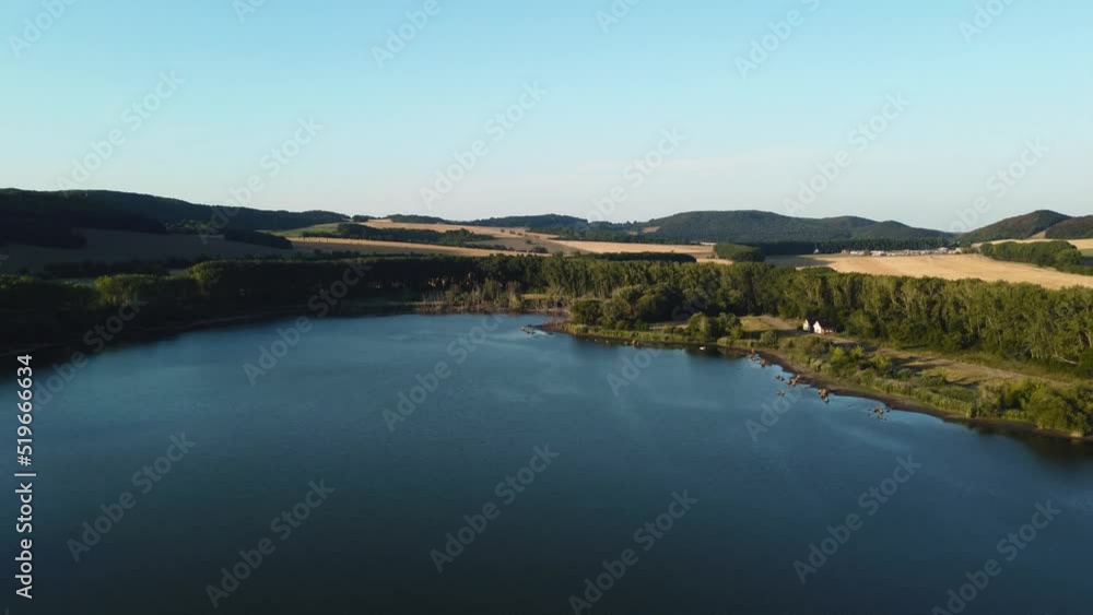 Drone flying backwards over the peaceful and idylic blue lake on sunset. Slowly and close flight above trees and lake with perfect aerial view from drone (UAV)in Europe - Slovakia. Drone flying backwards over the peaceful and idylic blue lake on sunset. Slowly and close flight above trees and lake with perfect aerial view from drone (UAV)in Europe - Slovakia.