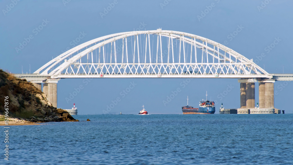 Breathtaking seascape with a white beautiful bridge with many moving cars above the water surface and sailing ships, time lapse effect. Shot. Calm sea with ripples, huge bridge, vessel and bue sky.