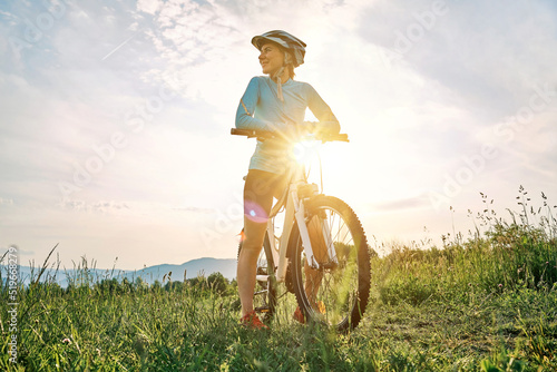 Fototapeta Naklejka Na Ścianę i Meble -  Cyclist Woman riding bike in helmets go in sports outdoors on sunny day a mountain in the forest. Silhouette female at sunset. Fresh air. Health care, authenticity, sense of balance and calmness.
