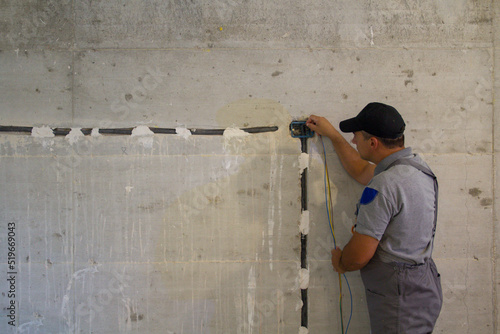 Image of a handyman electrician passing an electric probe through a corugate pipe on the construction site. Realization of an electrical system of a house. 