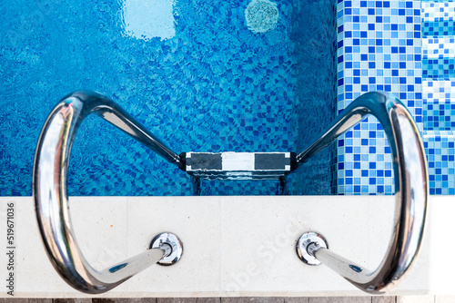 Steel ladder in the pool top view. Rubberized steps. blue ceramic tile mosaic in swimming pool