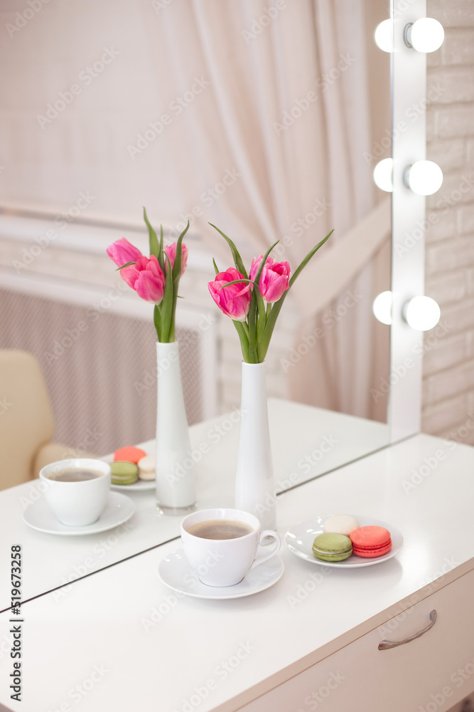 
Client's place in hairdressing and beauty salon with cup of coffee, macaroons and pink tulips in vase. 