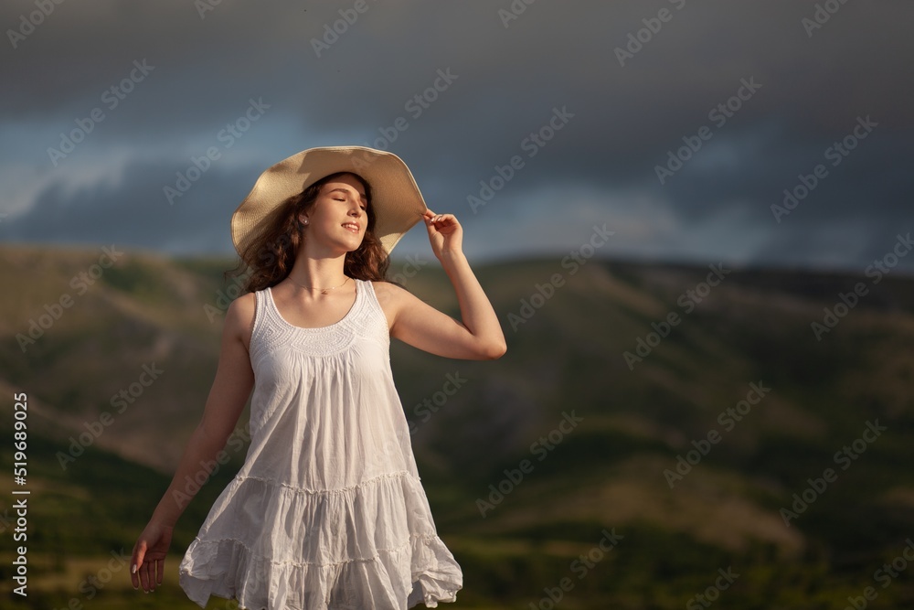 Woman in hat on the field with flowers on the landscape background