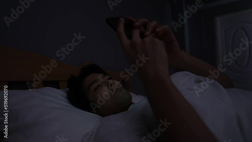 Holiday concept of 4k Resolution. Young Asian man playing mobile phone in bedroom.