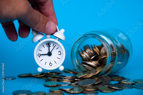 Scattered gold coins with hand holding alarm clock. Business concept photo