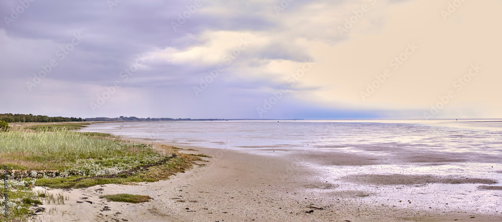 Beautiful, outdoors tidal and sand landscape at an empty beach in nature with clouds in the background. Outdoor natural view of sea water and green grass. Summer vacation day outside at the ocean.