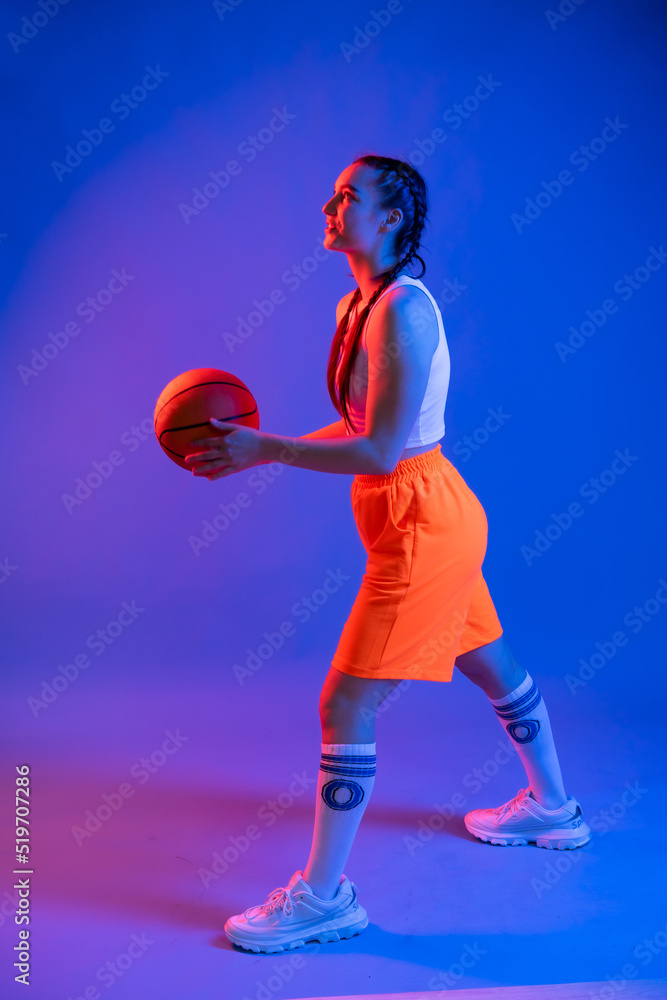a girl with a basketball in orange shorts, a t-shirt and a baseball cap. sportswoman in golfs and sneakers on a blue background. Physical education teacher. basketball player