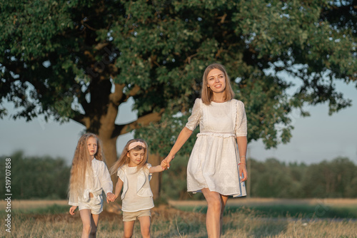 Harmonious relationship of mother with children. World Women's Day. Mom walks with the children in the village. Girls in a white dress with blonde hair