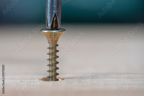 Golden screws screwed into wooden plank and screwdriver