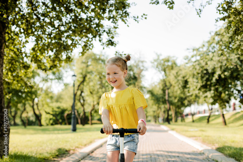 Portrait of a charming little girl riding a scooter in the park. Healthy lifestyle in childhood
