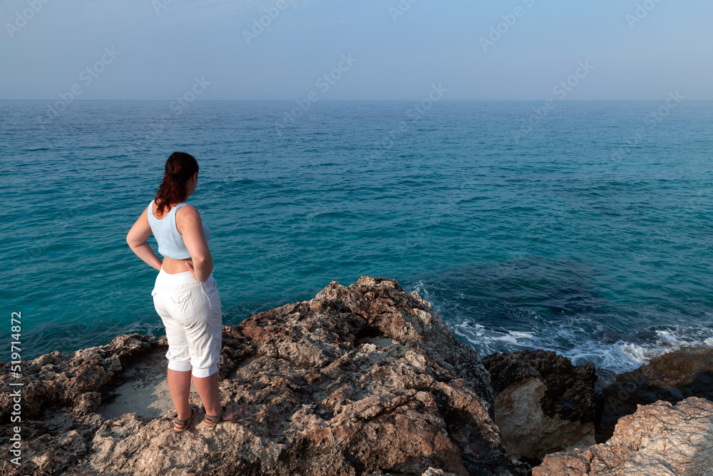 Young woman stands at the rocky coast
