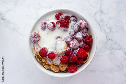 Bowl of multigrain cereal with yogurt and fresh raspberry berries on marble table background. Healthy diet breakfast. Top view, copy space 