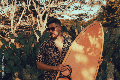 Obraz na płótnie Surfer z deską surfingową, idący wybrzeżem na naturalnym tle, drzewa i kaktusy. w salonie