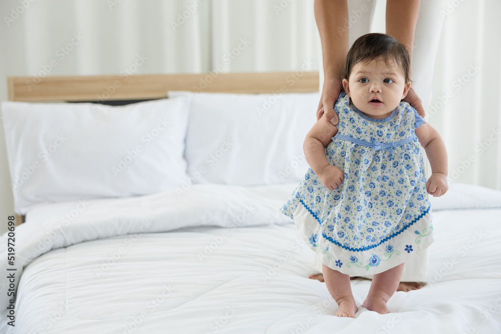 baby girl learning to walk and mother or sitter support her on bedroom baby girl learning to walk and mother or sitter support her on bedroom