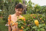 A lady in a yellow floral cropped top is appreciating the beauty of a large hibiscus in a garden full of blooms.